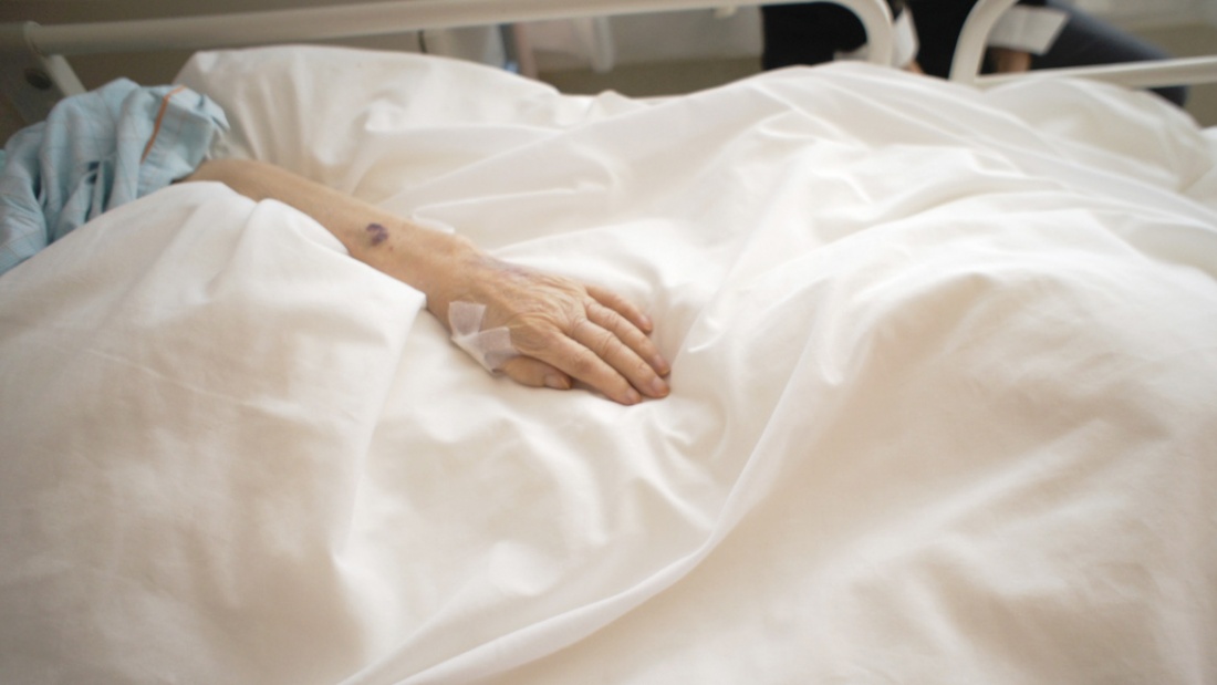 Die Hand einer kranken Frau ist auf der Bettdecke ihres Krankenbettes zu sehen.
