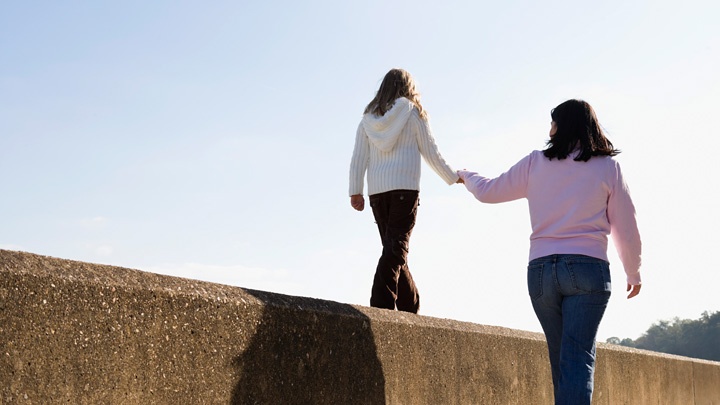 Ein Mädchen balanciert an der Hand ihrer Mutter auf einer Mauer. 