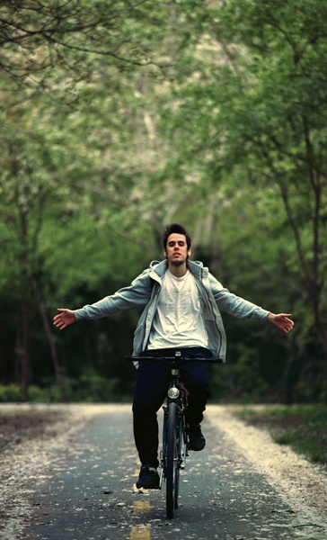 Junger Mann fährt mit ausgebreiteten Armen Fahrrad.