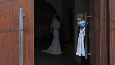 Frau mit Mund-Nasen-Bedeckung hält Tür geöffnet. 