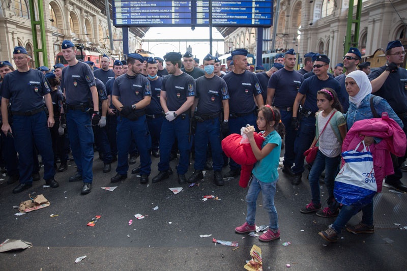 Eine Flüchtlingsfamilie verlässt den Bahnhof Budapest-Keleti. Aus den Bahnhofslautsprechern kommt währenddessen die Information, dass der Bahnhof geräumt und auf unbestimmte Zeit geschlossen bleiben wird.