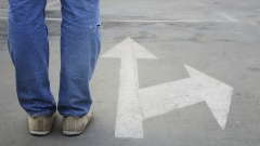 Ein Mann steht auf der Straße neben einem Pfeil, der zwei unterschiedliche Richtungen anzeigt.