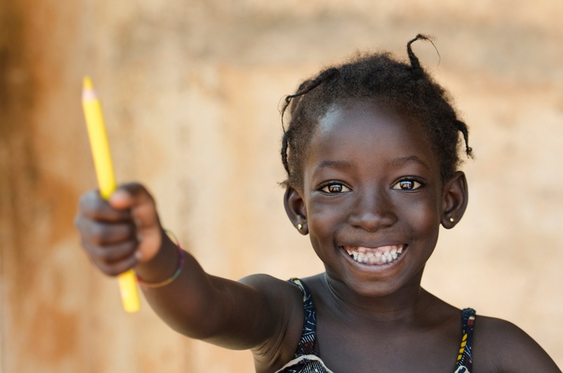 Ein kleines, afrikanisches Mädchen hält freudestrahlend einen gelben Stift in die Kamera