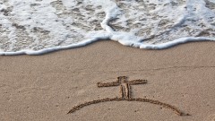 Ein in den Sand gemaltes Kreuz.