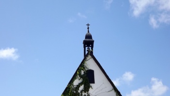 Kirchturmspitze mit Kreuz vor blauem Himmel.