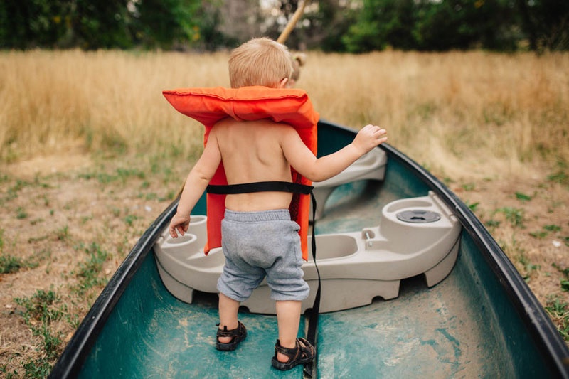 Junge steht mit Schwimmweste in einem Boot.