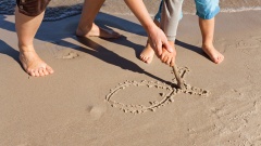 Ein Erwachsener und ein Kind zeichnen gemeinsam das Ichthys-Symbol in den Sand.