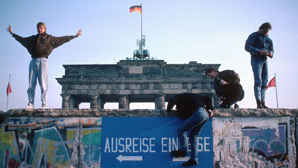 Am Tag nach der Maueröffnung stehen Menschen auf der Mauer vor dem Brandenburger Tor. 