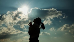 Silhouette einer Frau betet vor blauem Himmel mit Sonnenschein.