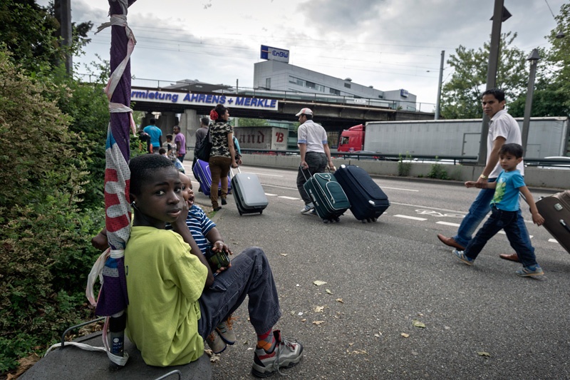 Flüchtlingskinder aus Afrika beobachten, wie die afghanische Flüchtlingsgruppe in Karlsruhe zur Landesaufnahmestelle für Flüchtlinge (LASt) geht.