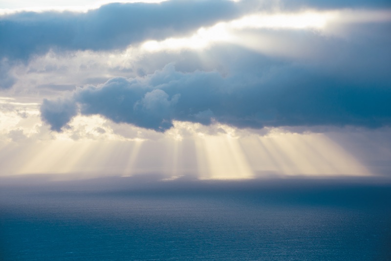 Sonnenstrahlen durchbrechen die Wolkendecke über dem Meer.