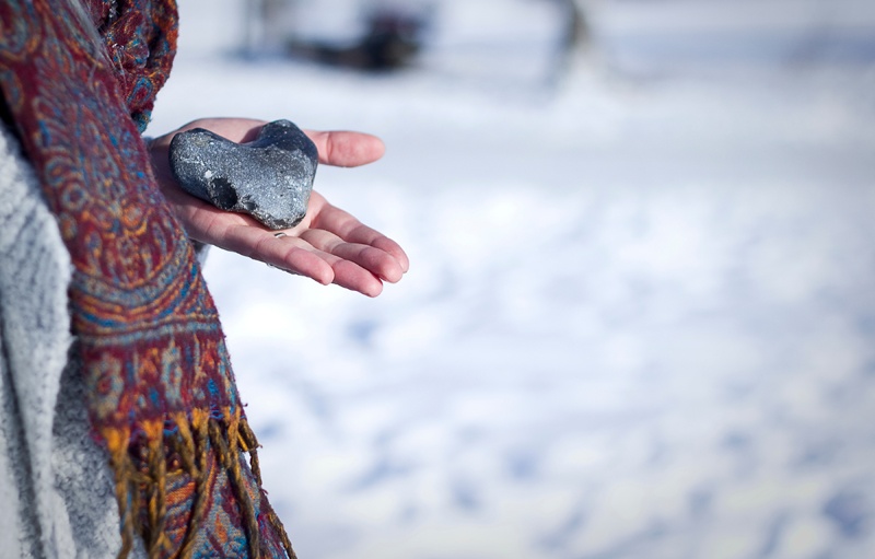 Frau vor einer Winterlandschaft mit einem herzförmigen Stein in der Hand.