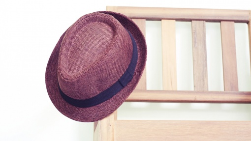 Ein Hut hängt an der Armlehne einer Holzbank.