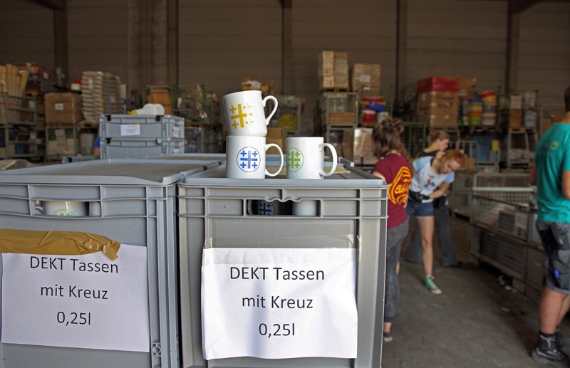 DEKT-Tassen stehen auf Boxen im Materiallager des Kirchentags in Berlin.